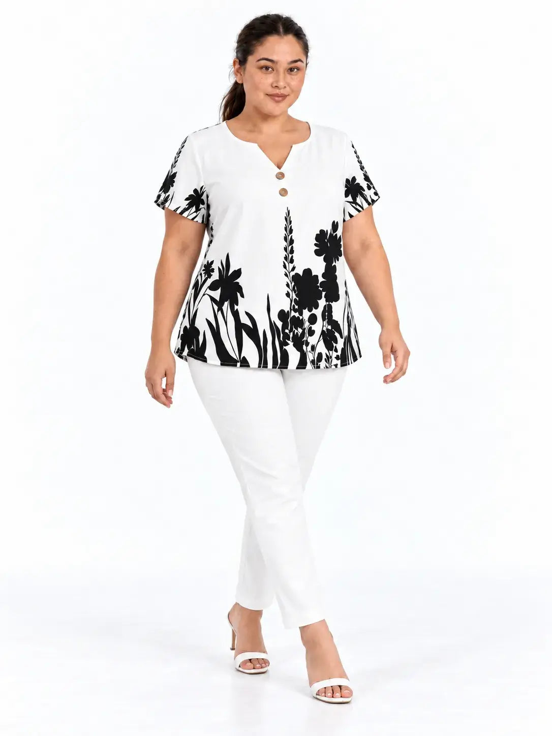 Blusa plus size floral preta e branca com mangas curtas tipo morcego, vista de frente em composição com calça branca.