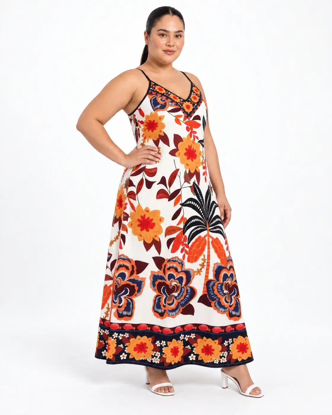Vestido longo plus size com flores coloridas e folhas pretas na modelo com a mão na cintura, em pose de frente.