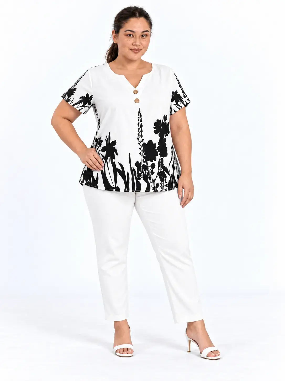 Modelo com a mão na cintura usando blusa plus size branca com estampa botânica preta, decote entalhado e mangas curtas.