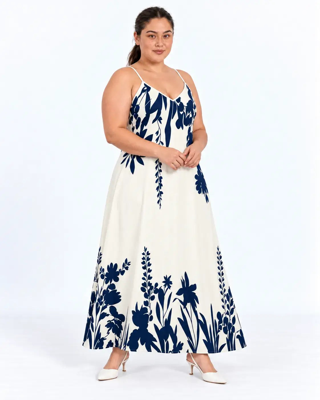Modelo em pose de três quartos com vestido longo plus size de fundo claro e estampa botânica azul-marinho.