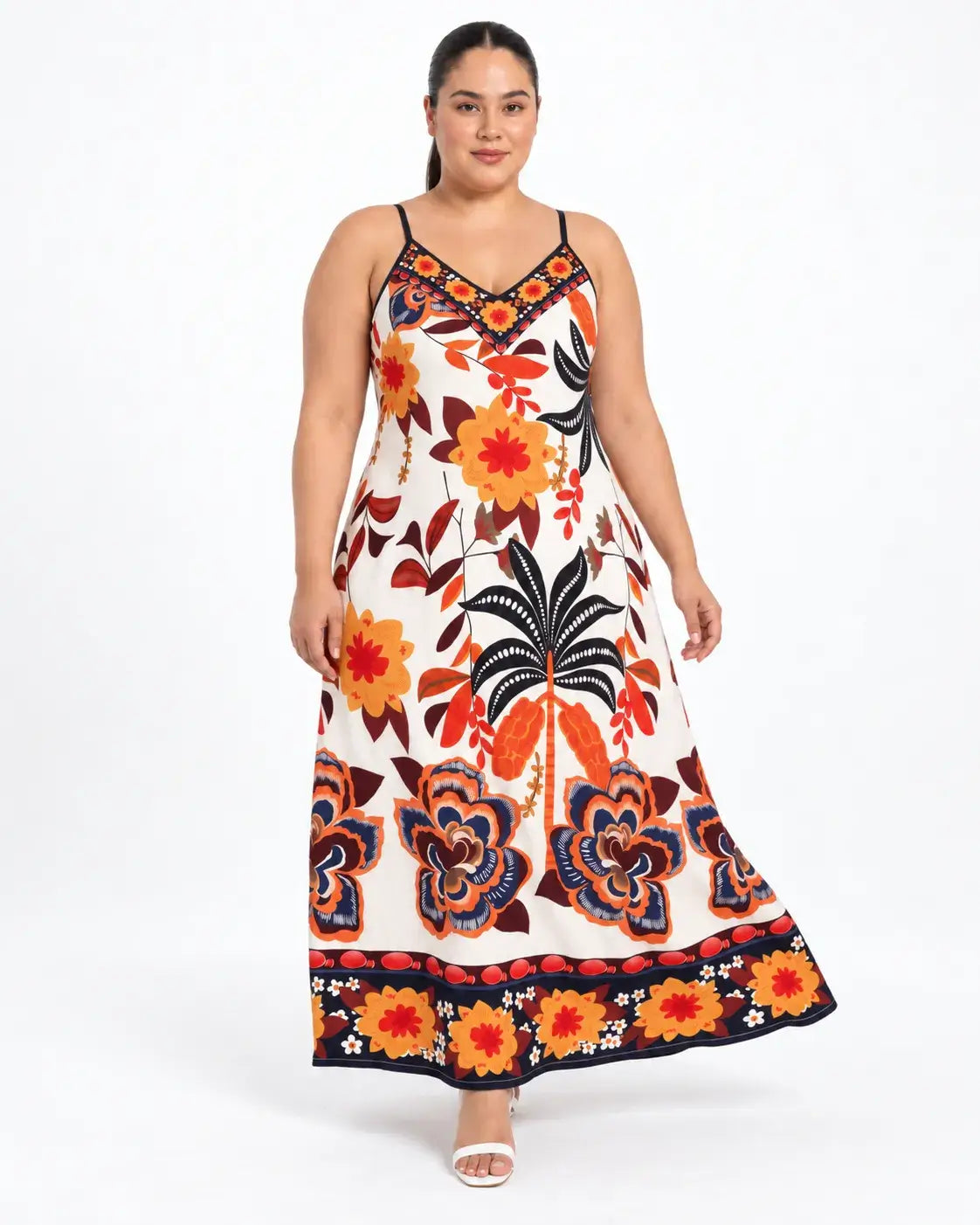Modelo dando um passo com vestido longo plus size de alças finas e estampa botânica multicolorida sobre fundo claro.