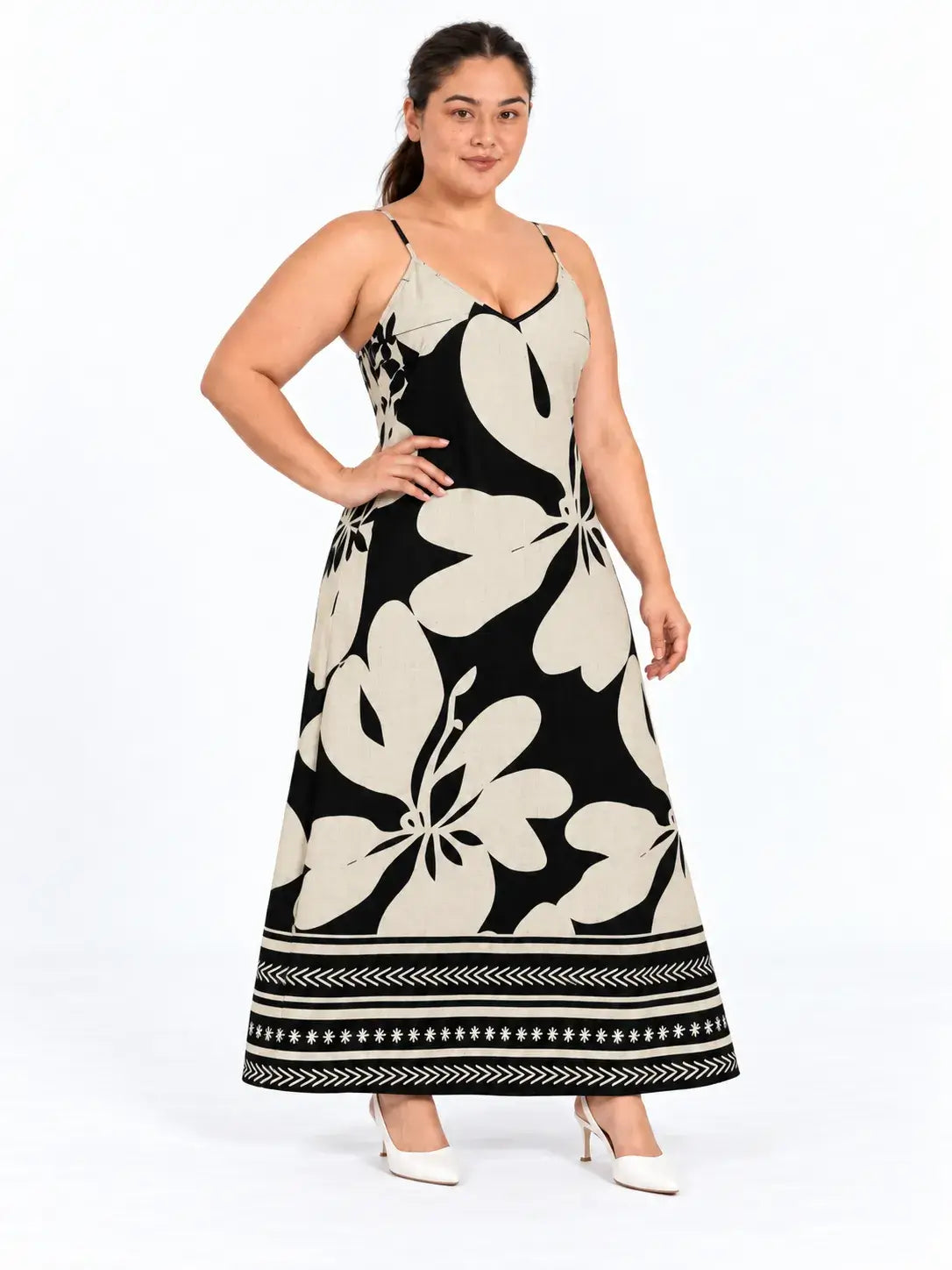 Vestido longo plus size floral boho bege e preto, com alças finas e decote em V, na modelo com a mão na cintura.